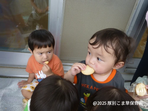 ベランダで遠足のおやつをおいしそうに食べているお子さまの様子