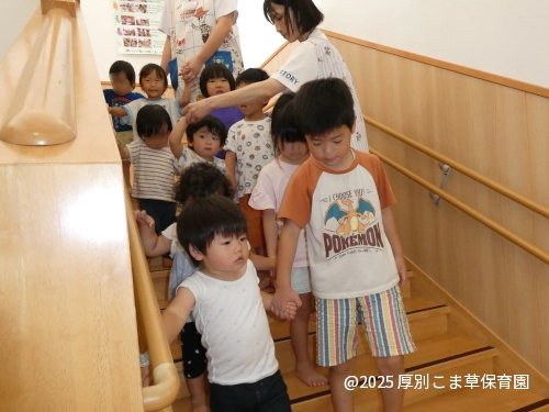 ひまわり組の子どもたちが１歳児の子どもたちに付き添って階段を下りる様子