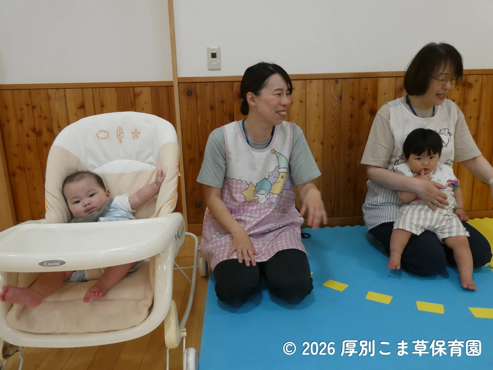 会場の後方で誕生会の様子を見ているたんぽぽ組（０歳児）の子どもたちの様子