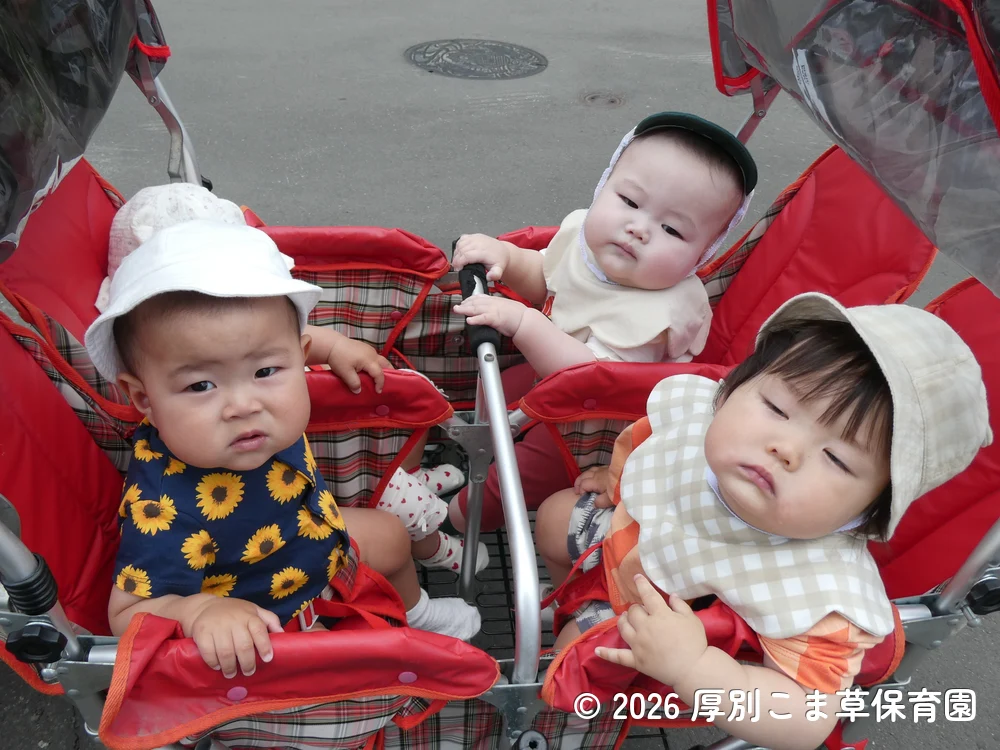 ４人乗りベビーカーに乗って遠足に出かけるたんぽぽ組（０歳児）の子どもたちの様子