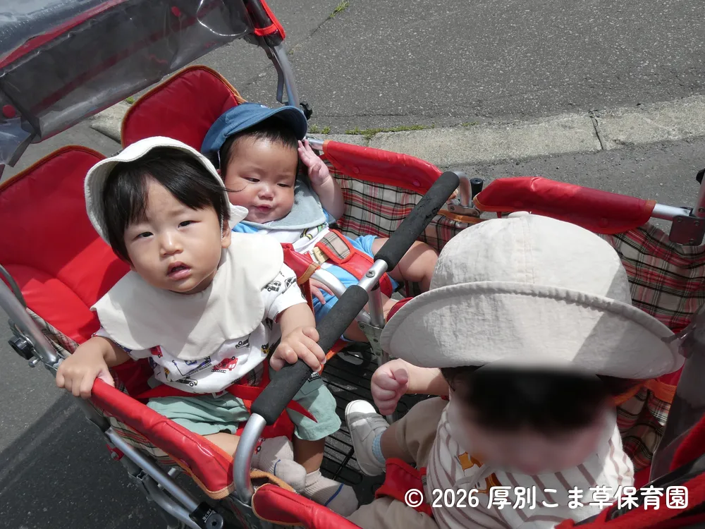 ４人乗りベビーカーに乗って遠足に出かけるたんぽぽ組（０歳児）の子どもたちの様子