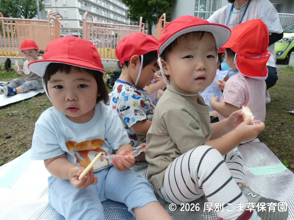 公園でおやつを食べているたんぽぽ組（１歳児）の子どもたちの様子