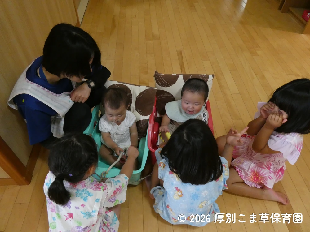 ワゴンカーに乗っておまつりを見学するたんぽぽ組(0歳児)と、一緒に遊ぶひまわり組(5歳児)の子どもたちの様子