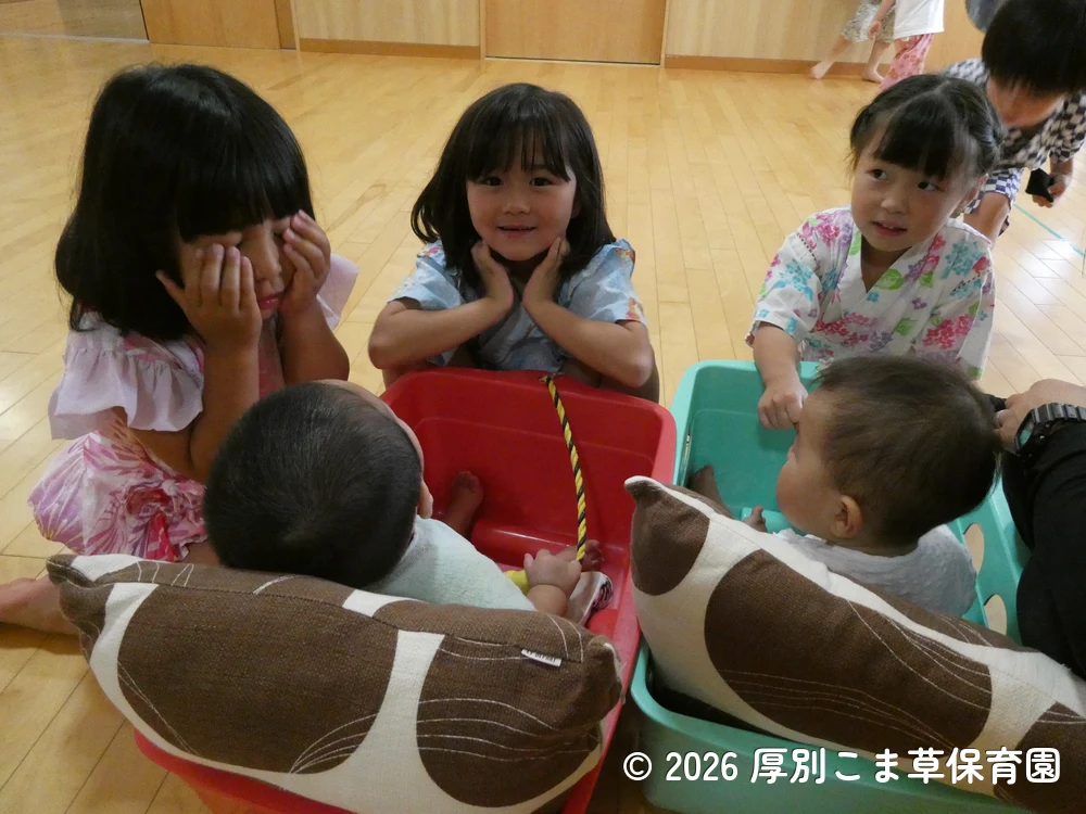 ワゴンカーに乗っておまつりを見学するたんぽぽ組(0歳児)と、一緒に遊ぶひまわり組(5歳児)の子どもたちの様子