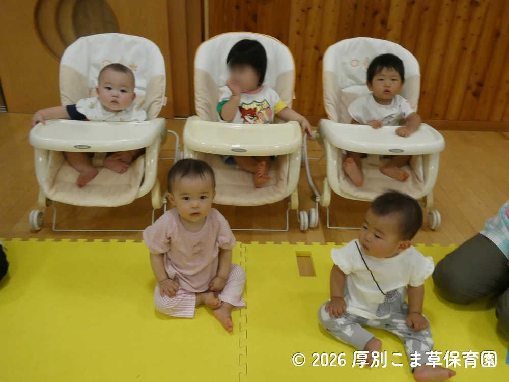 会場の後方から誕生会に参加しているたんぽぽ組（０歳児）の子どもたちの様子